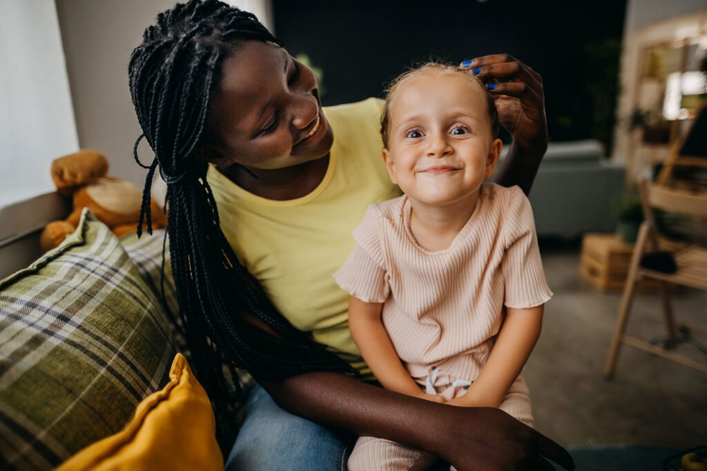 a young girl smiles at the camera while her foster parent embraces her